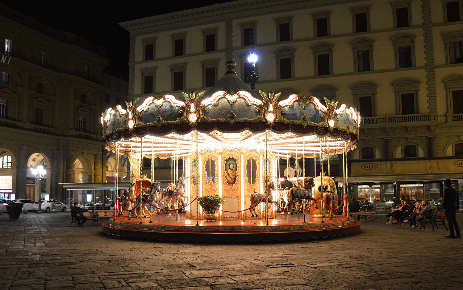 FLORENCE, ITALY - MARCH 15, 2017: Carousel at night iluminated in the middle of the square in Florence. Unidentified tourists waiting around
